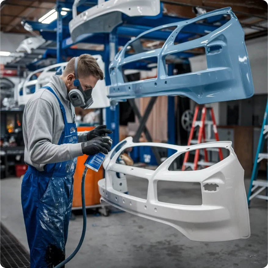 Technician spray-painting vehicle bumpers in an auto workshop — representing automotive logistics, aftermarket parts distribution, and transport coordination.